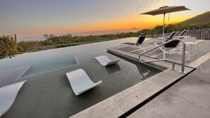 An infinity pool with lounge chairs and an umbrella, overlooking a scenic landscape during sunset. - Exclusive Solaria Arch View Penthouse with Jacuzzi (Cabo San Lucas)