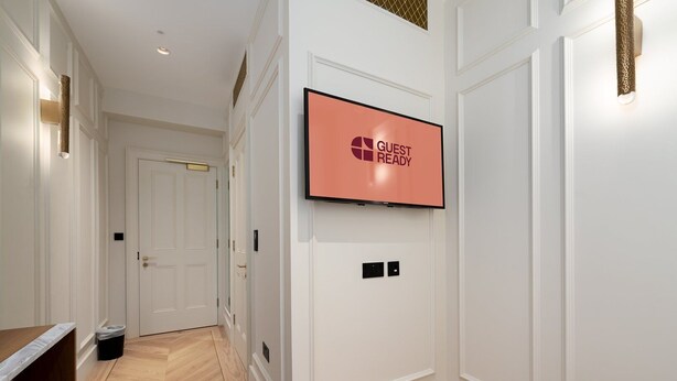 A hallway with a flat-screen TV mounted on the wall displaying "GUEST READY". - GuestReady - Fitzrovia Comfort (London)