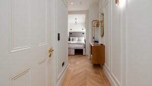 A hallway leading to a bedroom with a bed, bedside table, and a mirror. - GuestReady - Fitzrovia Comfort (London)