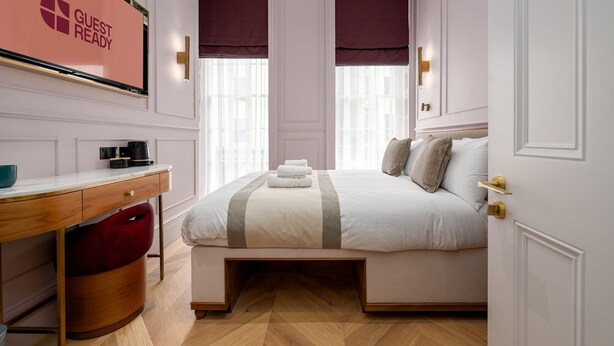 A hotel room with a bed, a desk, a chair, and a window with a view. - GuestReady – Chic Retreat in Fitzrovia (London)