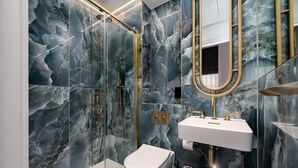 A modern bathroom with a glass-enclosed shower, a white toilet, and a gold-framed mirror. - GuestReady – Chic Retreat in Fitzrovia (London)