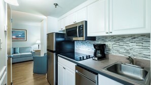 A modern kitchen with white cabinets, a stainless steel refrigerator, a microwave, and a coffee maker. - Spacious One Bedroom Condo (Virginia Beach)