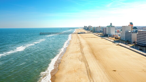 A beach with a pier extending into the ocean, adjacent to a row of hotels with balconies overlooking the sea. - Spacious One Bedroom Condo (Virginia Beach)