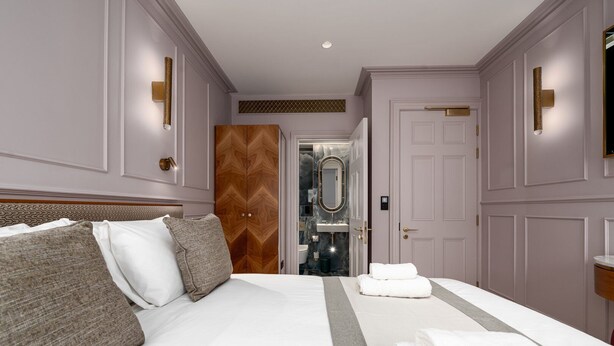 A hotel room with a large bed, a wardrobe, a bathroom with a mirror, and a door leading to another room. - GuestReady - Elegant stay in Fitzrovia (London)