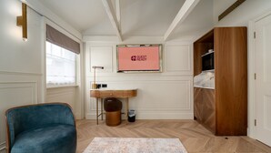 A hotel room with a wooden wardrobe, a desk with a chair, a trash bin, and a framed sign on the wall. - GuestReady – Top Floor Central London Getaway (London)