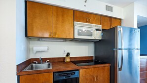 A compact kitchen with wooden cabinets, a stainless steel refrigerator, a microwave, and a dishwasher. - One Bedroom Condo, Oceanside! (Virginia Beach)