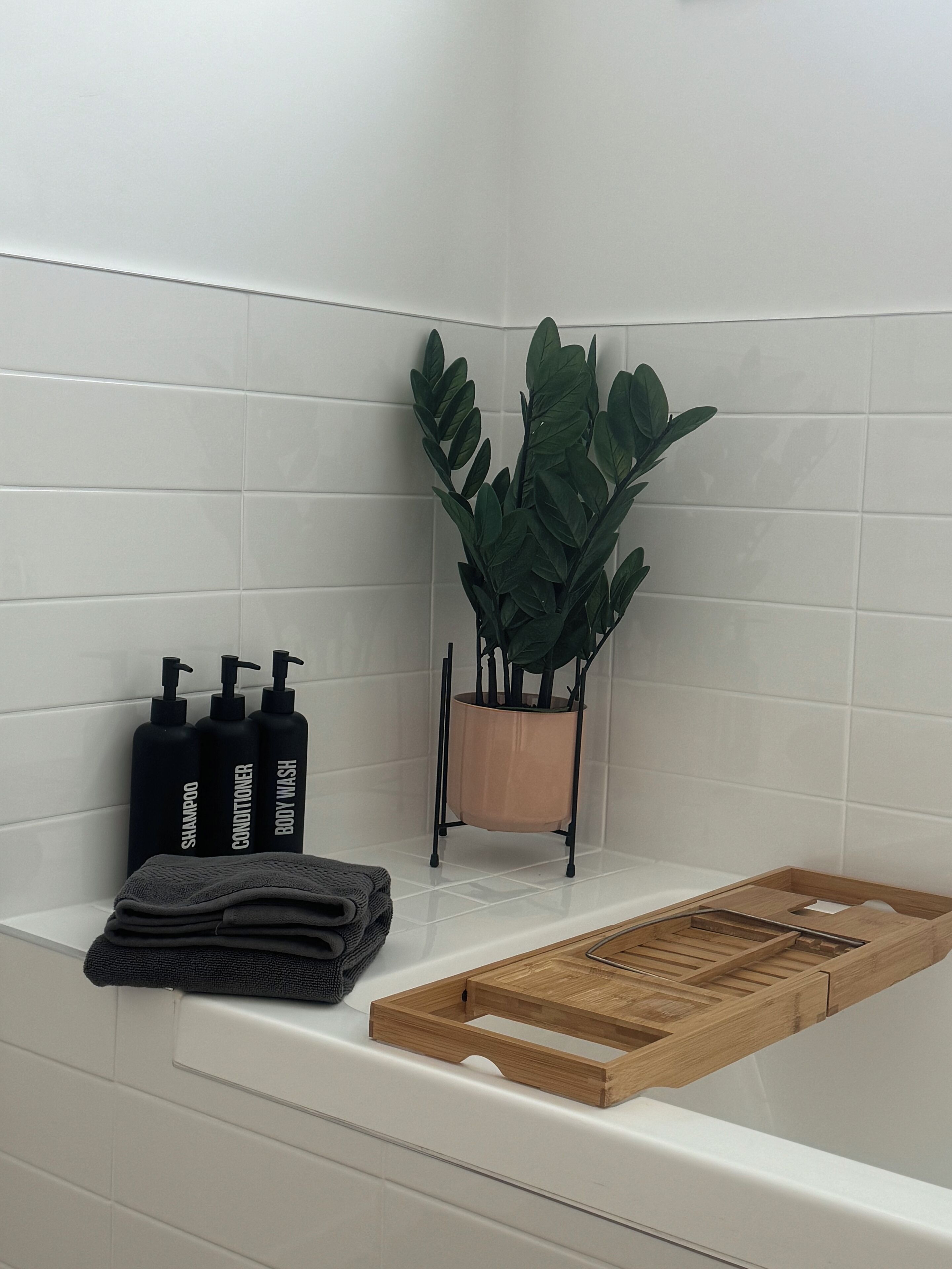 A bathroom with white tiles, a potted plant, and toiletries.