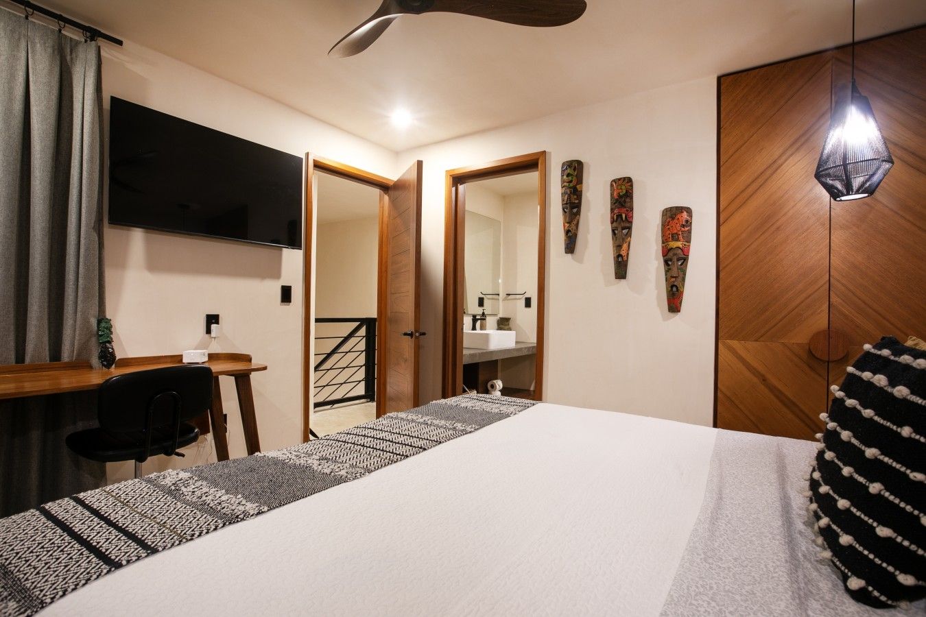 A bedroom with a bed, a desk, a chair, a television, a mirror, and a wardrobe.