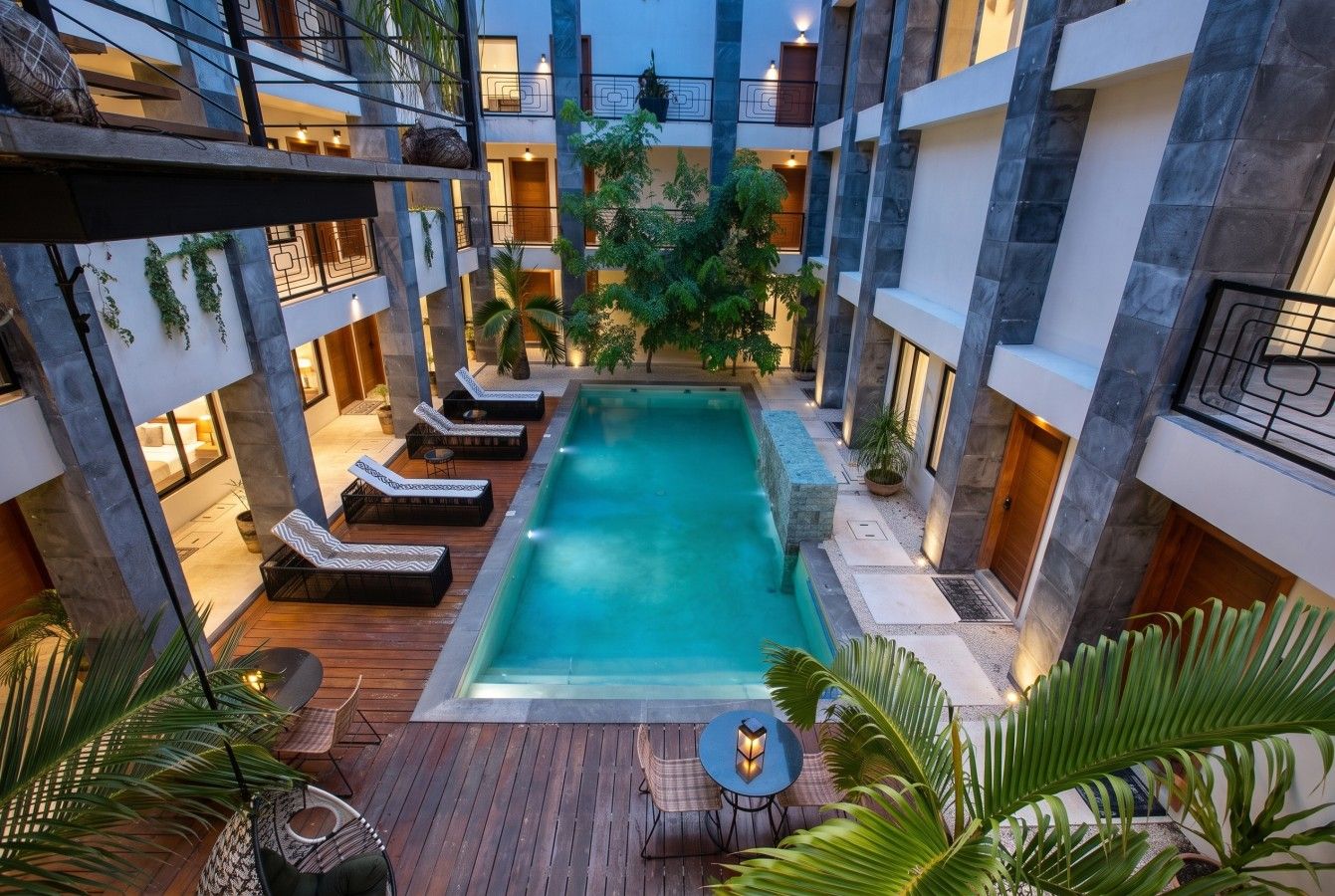 A multi-level building with a central swimming pool, lounge chairs, and potted plants.