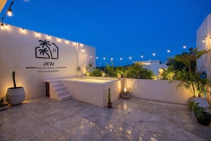 A rooftop patio area with a white wall featuring a logo and text for JKW Vacation Club, a staircase, and string lights.