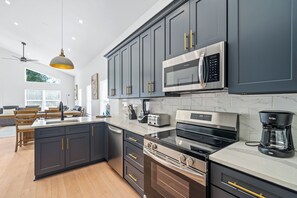 A modern kitchen with dark cabinets, a large island, stainless steel appliances, and a dining area with wooden furniture. - Spacious 4-bedroom house in charming Foley (Foley)