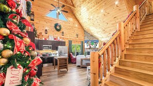 A cozy cabin interior with a wooden staircase, a decorated Christmas tree, and a kitchen area. - XmasCabins by SmokyStays - Christmas Themed Year Round (Pigeon Forge)