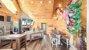A cozy log cabin interior with a dining area, kitchen, and fireplace. - XmasCabins by SmokyStays - Christmas Themed Year Round (Pigeon Forge)