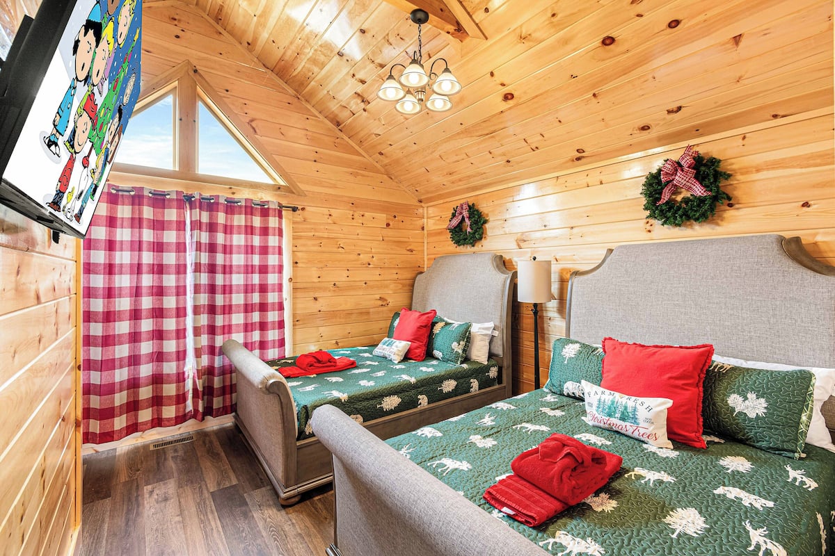 Una habitación acogedora tipo cabaña con dos camas, cortinas de cuadros y ropa de cama con motivos navideños.