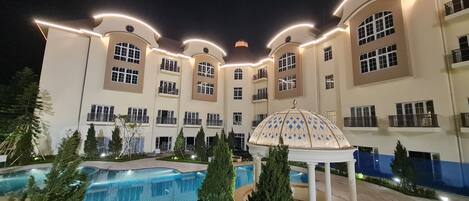 A multi-story hotel with a swimming pool, a gazebo, and a crescent moon in the sky.