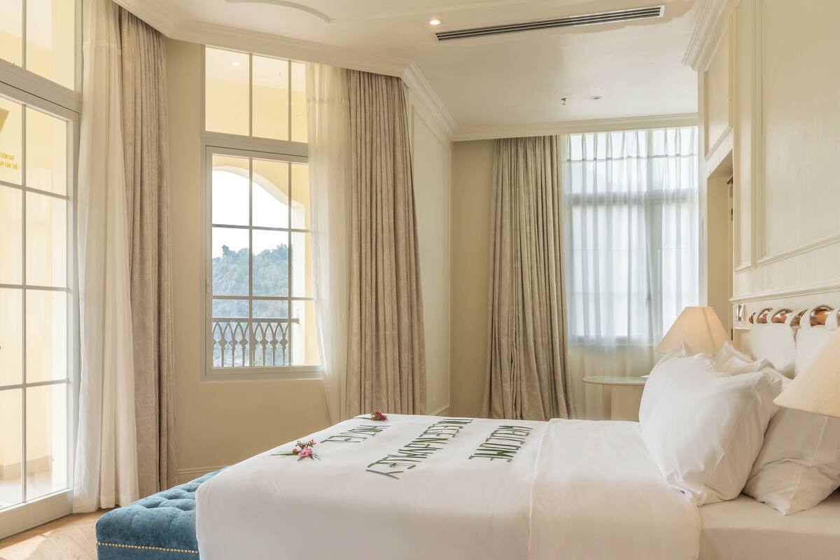 Une chambre spacieuse avec un grand lit, une petite table de chevet, une chaise et une vue sur l’extérieur par une fenêtre.