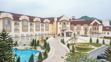 A hotel with a swimming pool, landscaped gardens, and a parking area.