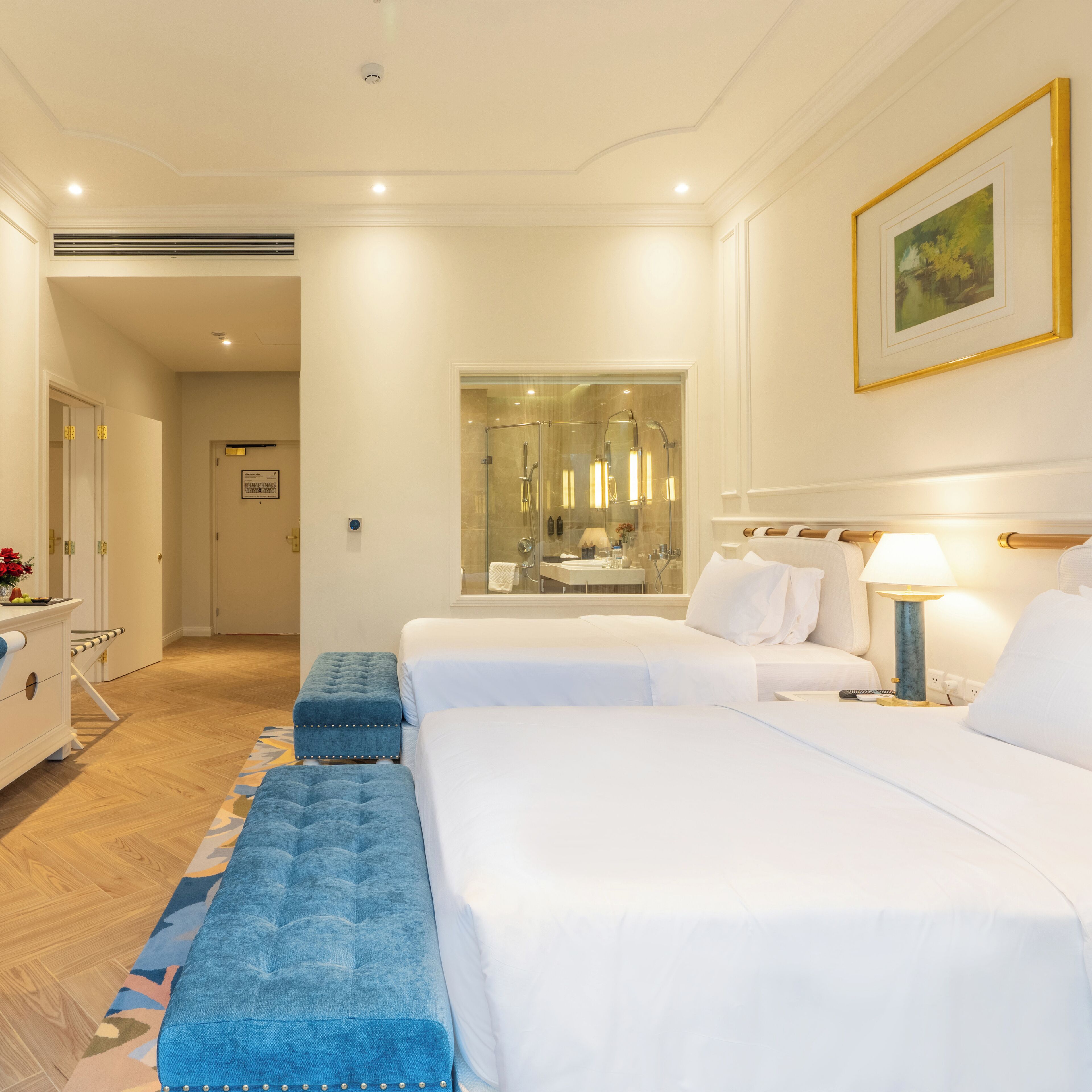 Una camera d'albergo con due letti, un grande specchio, un bagno con doccia e una scrivania con lampada.