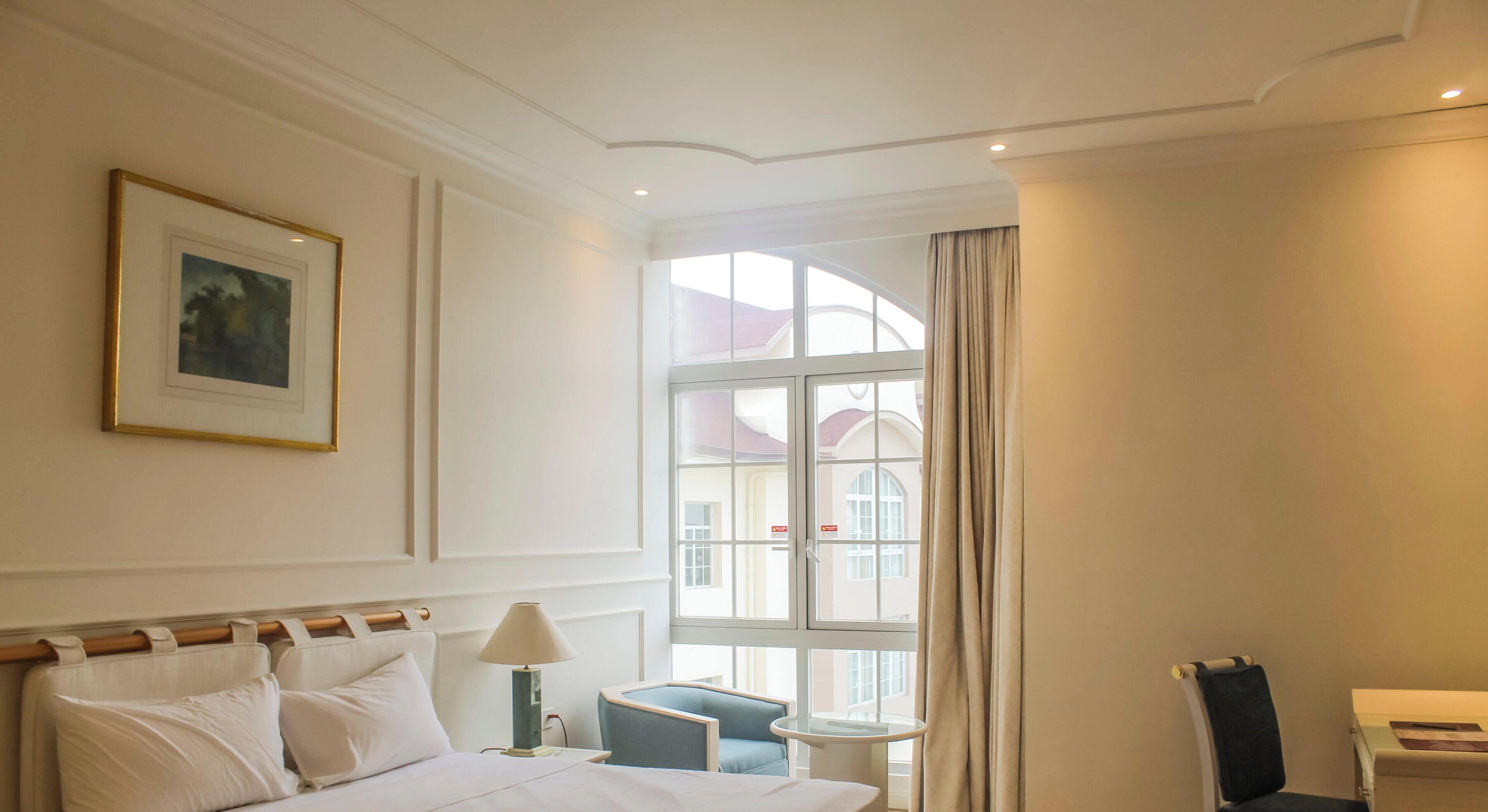 A hotel room with a bed, a bedside table, a lamp, a chair, and a window with curtains.