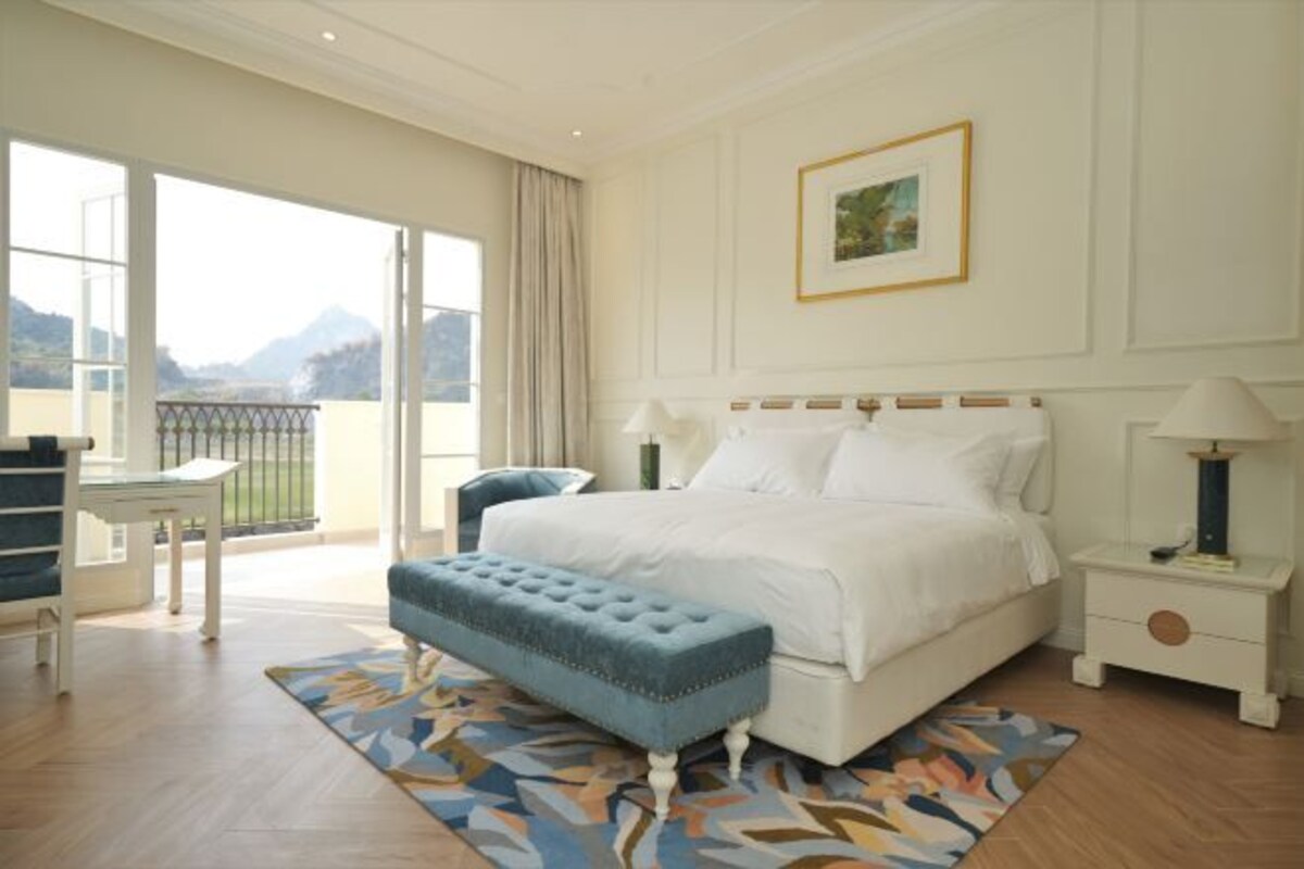 A bedroom with a large bed, a bedside table, a chair, and a view of the outdoors.