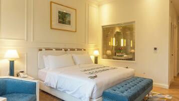 Ein Hotelzimmer mit einem großen Bett, einem blauen Sessel, einer Bank, einem Gemälde an der Wand und einem Spiegel über dem Bett.