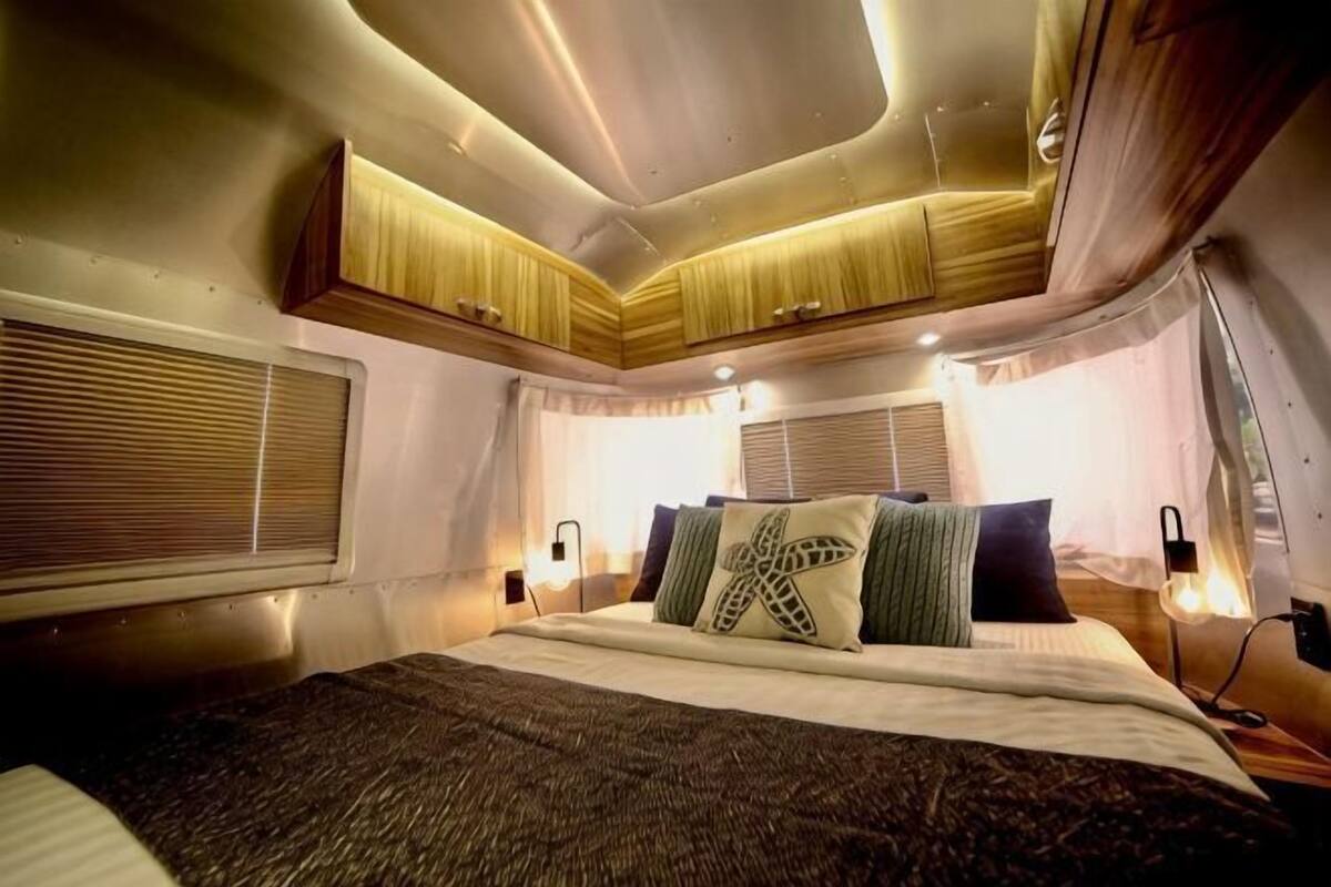 Un dormitorio con cama, mesitas de noche, cortinas y una ventana.