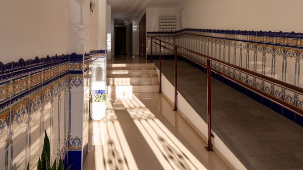 Un couloir aux murs recouverts de carreaux décoratifs, doté d’un sol en marbre et d’une main courante.