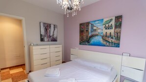 Une chambre à coucher comprenant un lit, une commode, un tableau représentant un paysage de canal et un lustre.