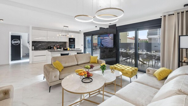 A modern living room with a sofa, coffee table, and a dining area with a TV. - 6 bedroom stunning home in Podglavica (Podglavica)