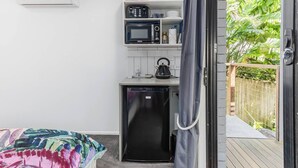 A compact kitchen with a microwave, toaster, and kettle, a small refrigerator, and a shelf with kitchenware. - Lilys Studio (Kingscliff)
