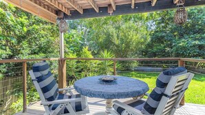 A covered outdoor seating area with a round table and two chairs, surrounded by lush greenery. - Lilys Studio (Kingscliff)