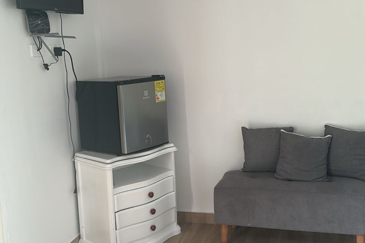 Une pièce dotée d’un téléviseur à écran plat fixé au mur, d’un meuble de rangement blanc avec des tiroirs, d’un canapé gris et d’un plancher en bois.