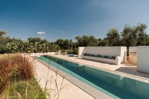 Piscina con deck blanco, zona de estar y vistas a olivos.