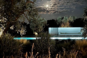 A modern outdoor pool area with a minimalist pool table and surrounding greenery.