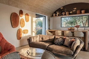 A modern living room with a sofa, a coffee table, and a dining area with chairs and a kitchen counter.