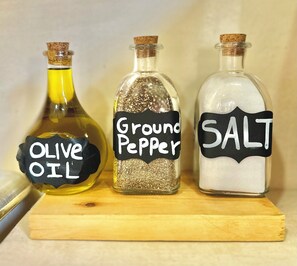 Three glass bottles with cork stoppers labeled 'Olive Oil,' 'Ground Pepper,' and 'Salt' on a wooden surface. - JOSE CONDOS BOUTIQUE HOTEL (Tulum)