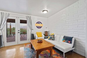 A modern living room with a white brick wall, a white sofa, a wooden coffee table, and a glass door leading to an outdoor patio.