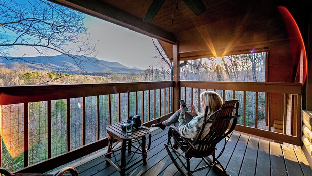 Terraza de madera con una mecedora y una mesa, con vistas a un paisaje montañoso.