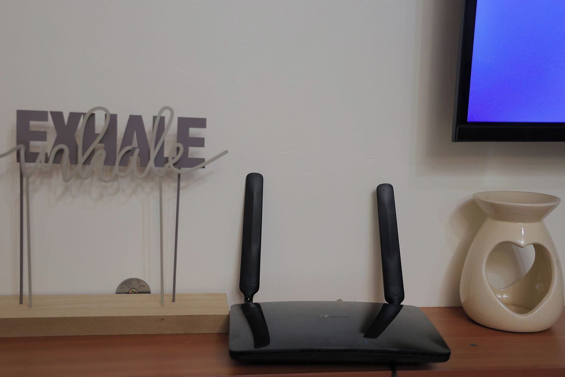 A router on a wooden table with a decorative sign saying "EXHAVE" and a TV mounted on the wall.