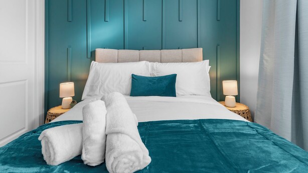 A neatly made bed with white and teal bedding, two bedside lamps, and a teal headboard. - Classy | Stylish | 13 min to West Edmonton Mall (Edmonton)