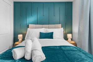 Un lit bien fait, avec une literie blanche et turquoise, deux lampes de chevet et une tête de lit turquoise.