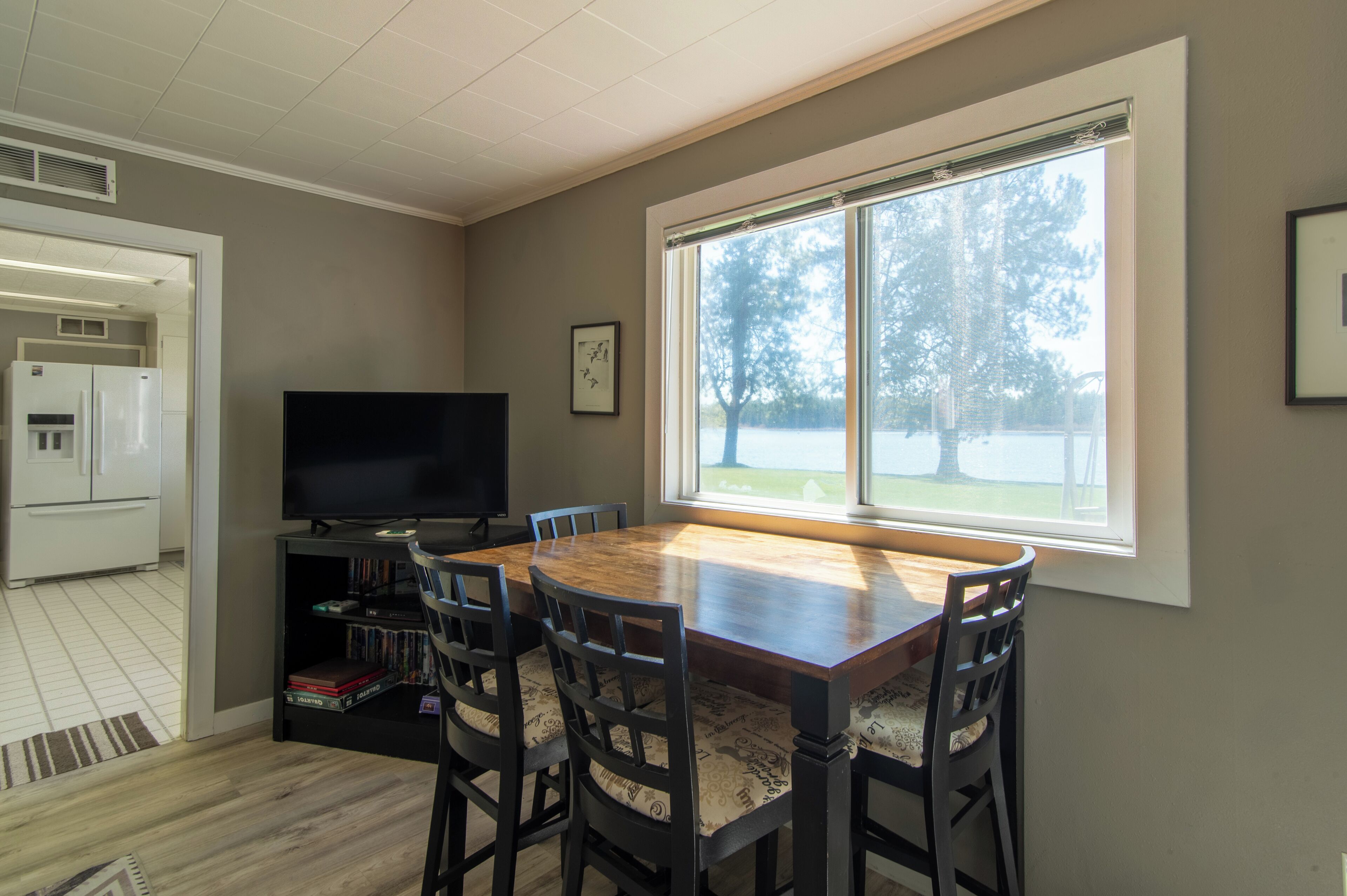 Un comedor con una mesa y sillas de madera, un televisor y un refrigerador al fondo.