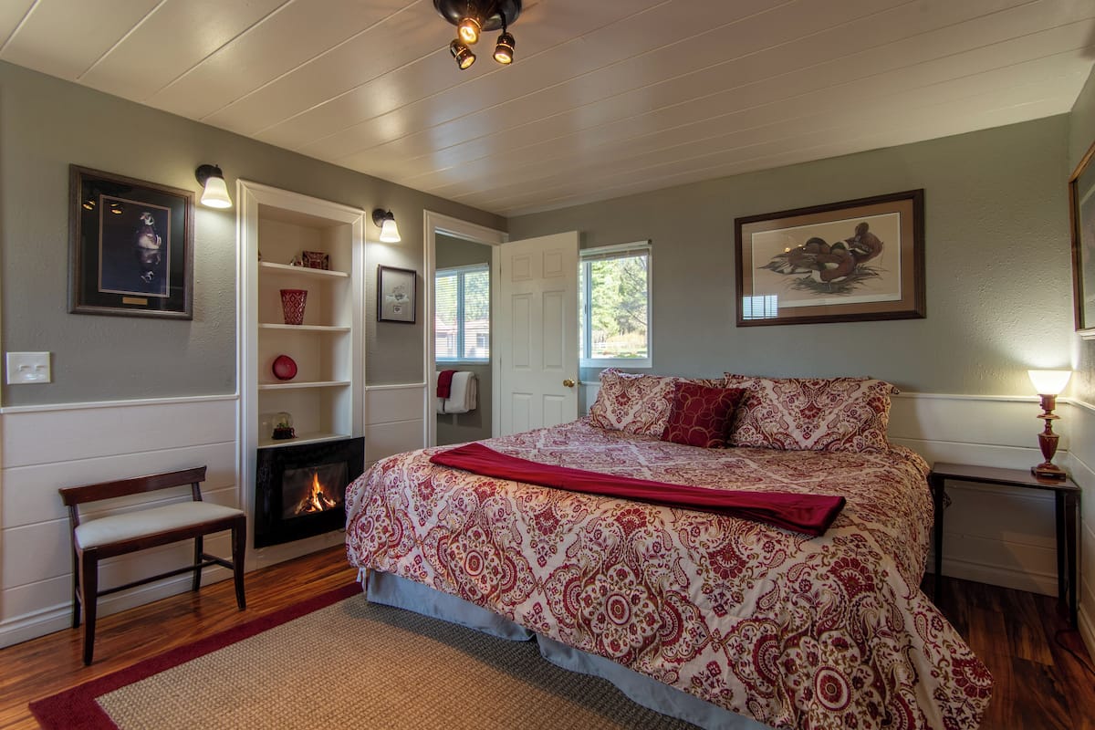 A bedroom with a large bed, a fireplace, a bench, and a door leading to another room.