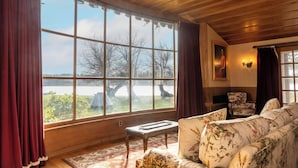 A room with a large window, wooden ceiling, a floral sofa, a small table, and a chair. - Historic  Gilchrist Waterfront Resort (Crescent)