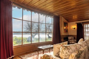 Una habitación con un ventanal grande, techo de madera, un sofá floral, una mesita y una silla.