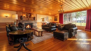 A spacious living room with leather furniture, a fireplace, and large windows. - Historic  Gilchrist Waterfront Resort (Crescent)