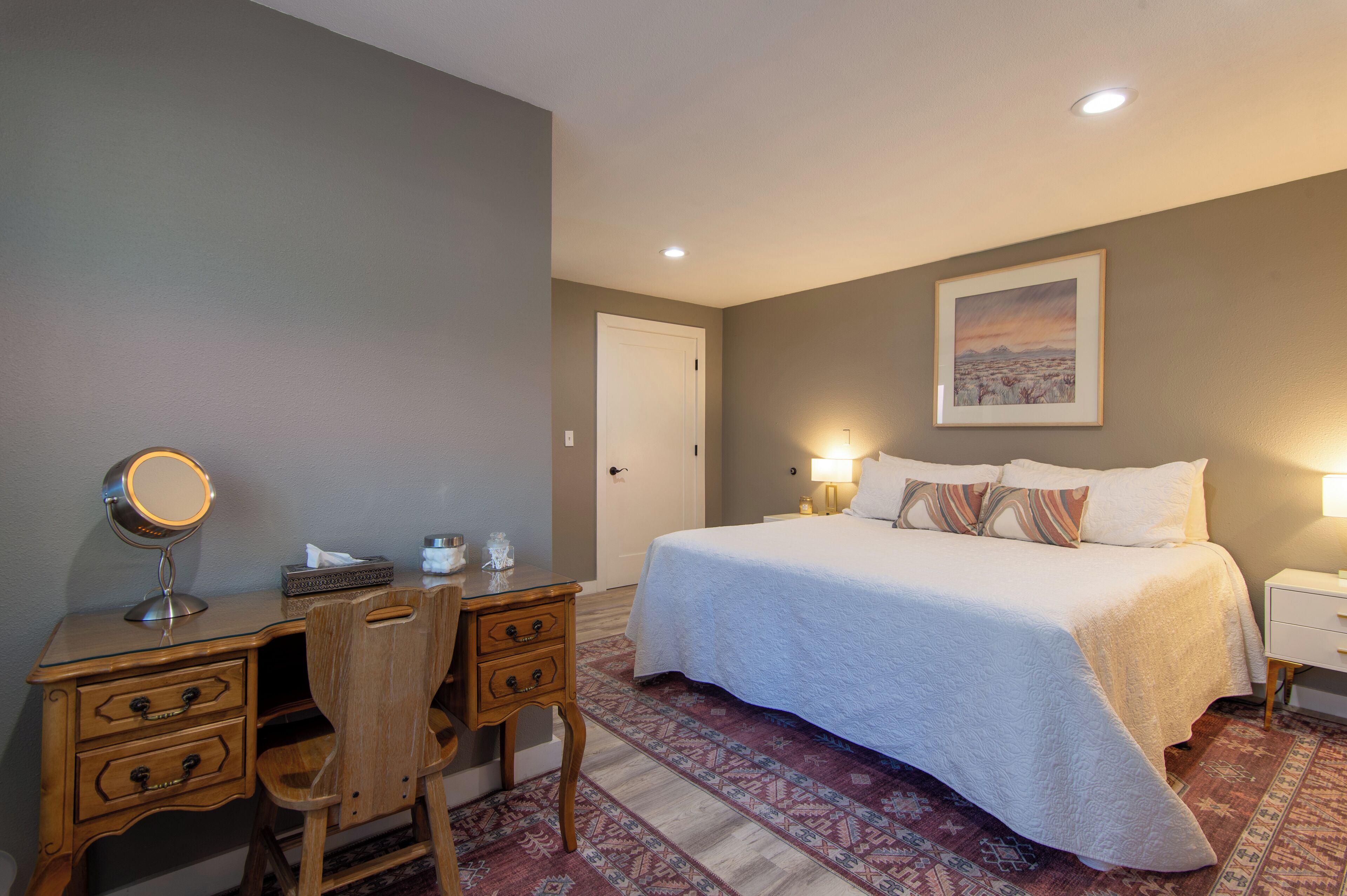A bedroom with a bed, bedside tables, a desk with a mirror, and a chair.