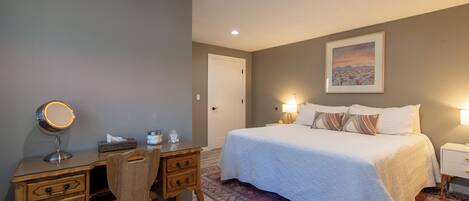 A bedroom with a bed, bedside tables, a desk with a mirror, and a chair.