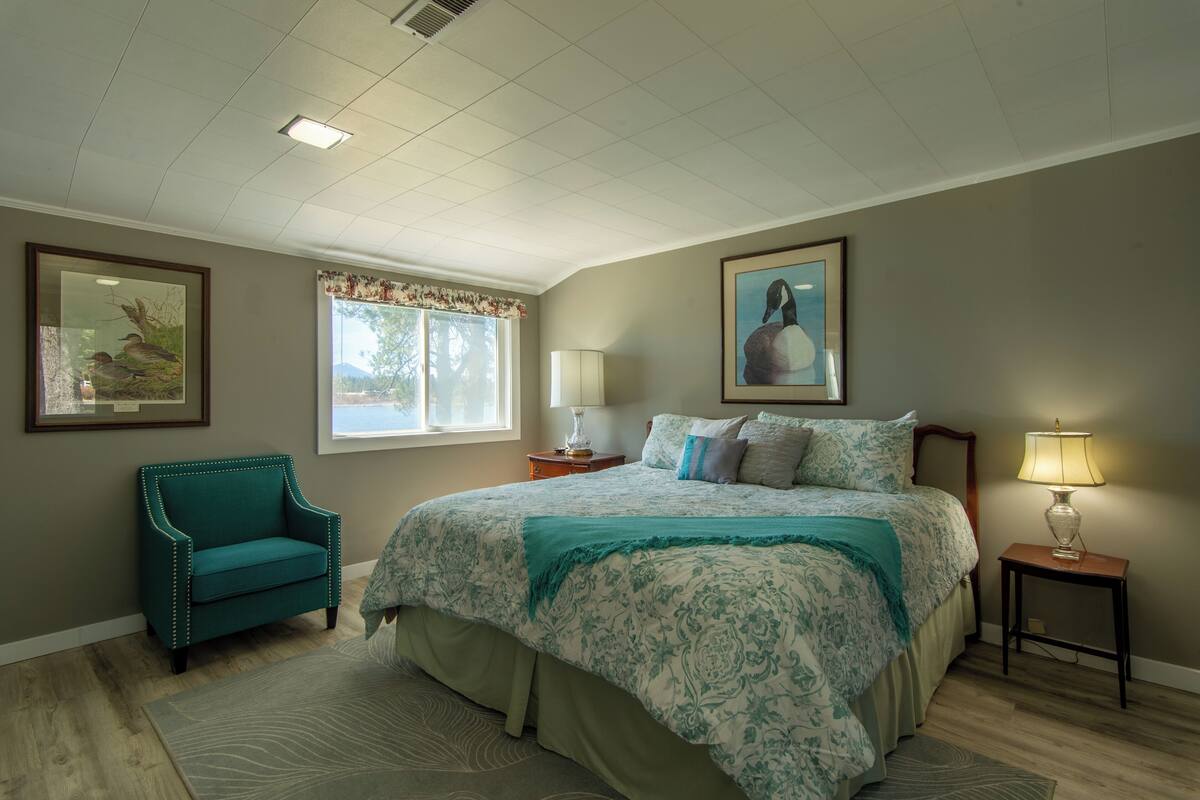 A bedroom with a large bed, a chair, a window with curtains, and two lamps.