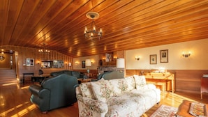 A spacious living room with a wooden ceiling, a floral sofa, a green armchair, and a dining area with wooden furniture. - Historic  Gilchrist Waterfront Resort (Crescent)